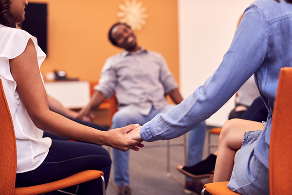 Multicultural group joining hands during mental health group therapy